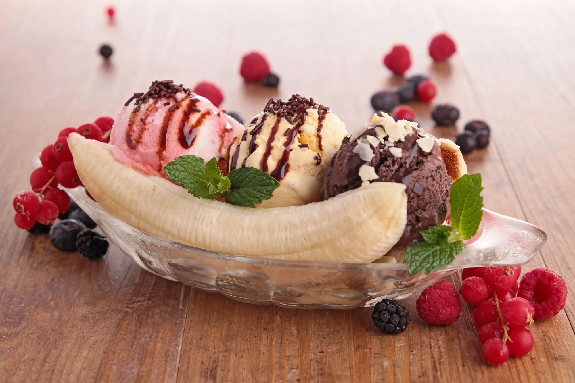 A banana split with three scoops, chocolate sauce and fresh berries