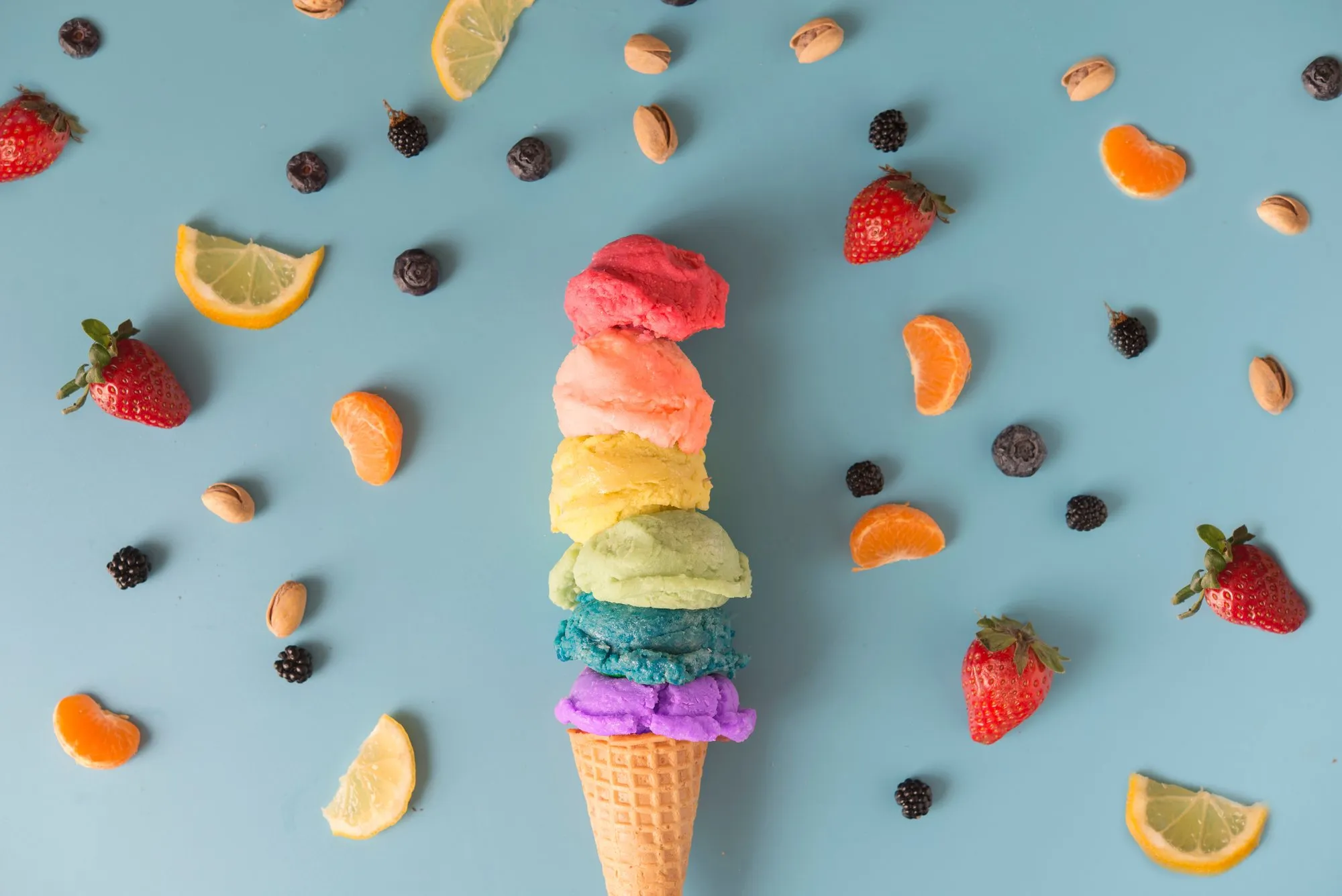 A rainbow ice cream cone surrounded by fresh fruit