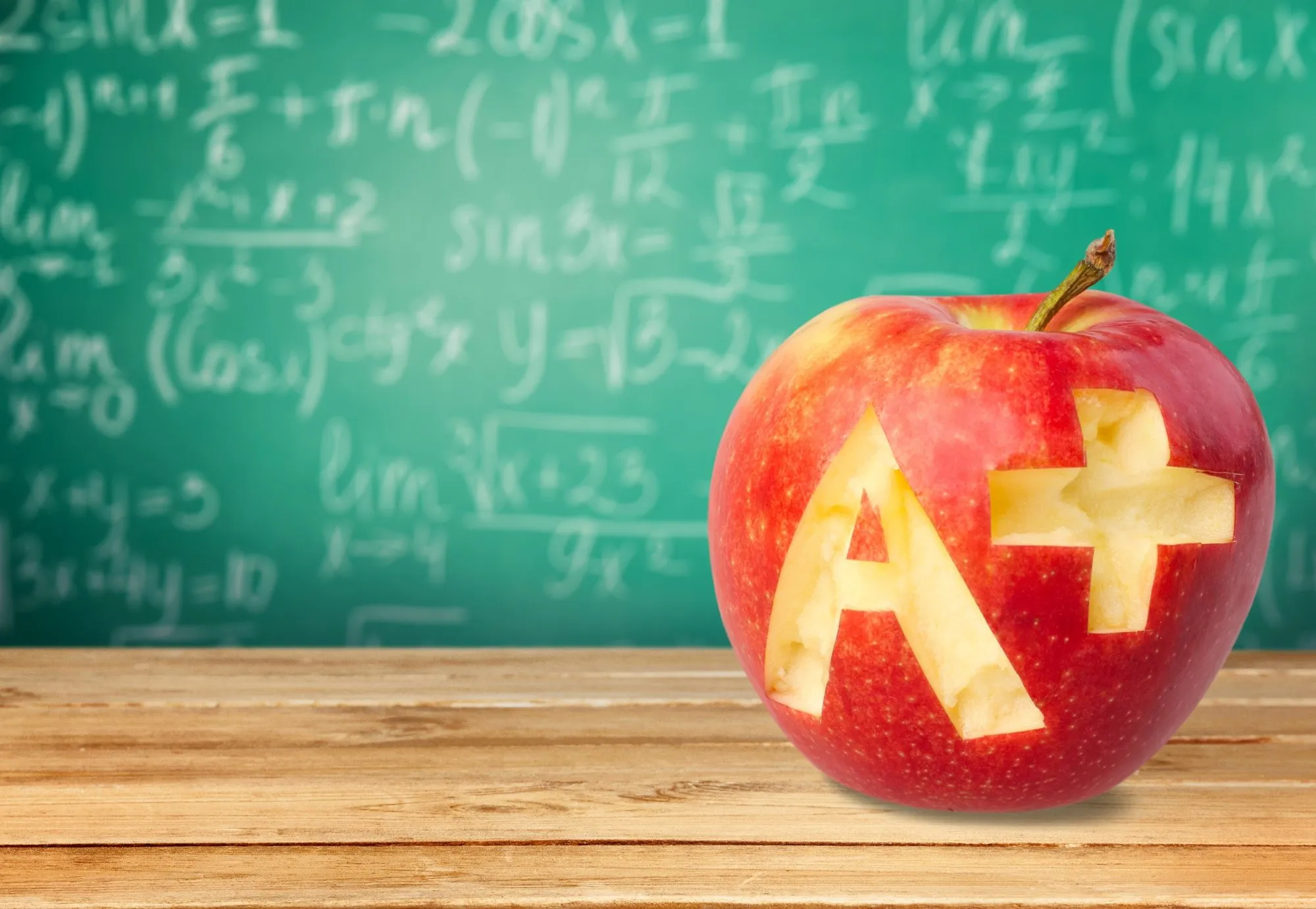 An apple with an A+ carved into it in front of a chalkboard